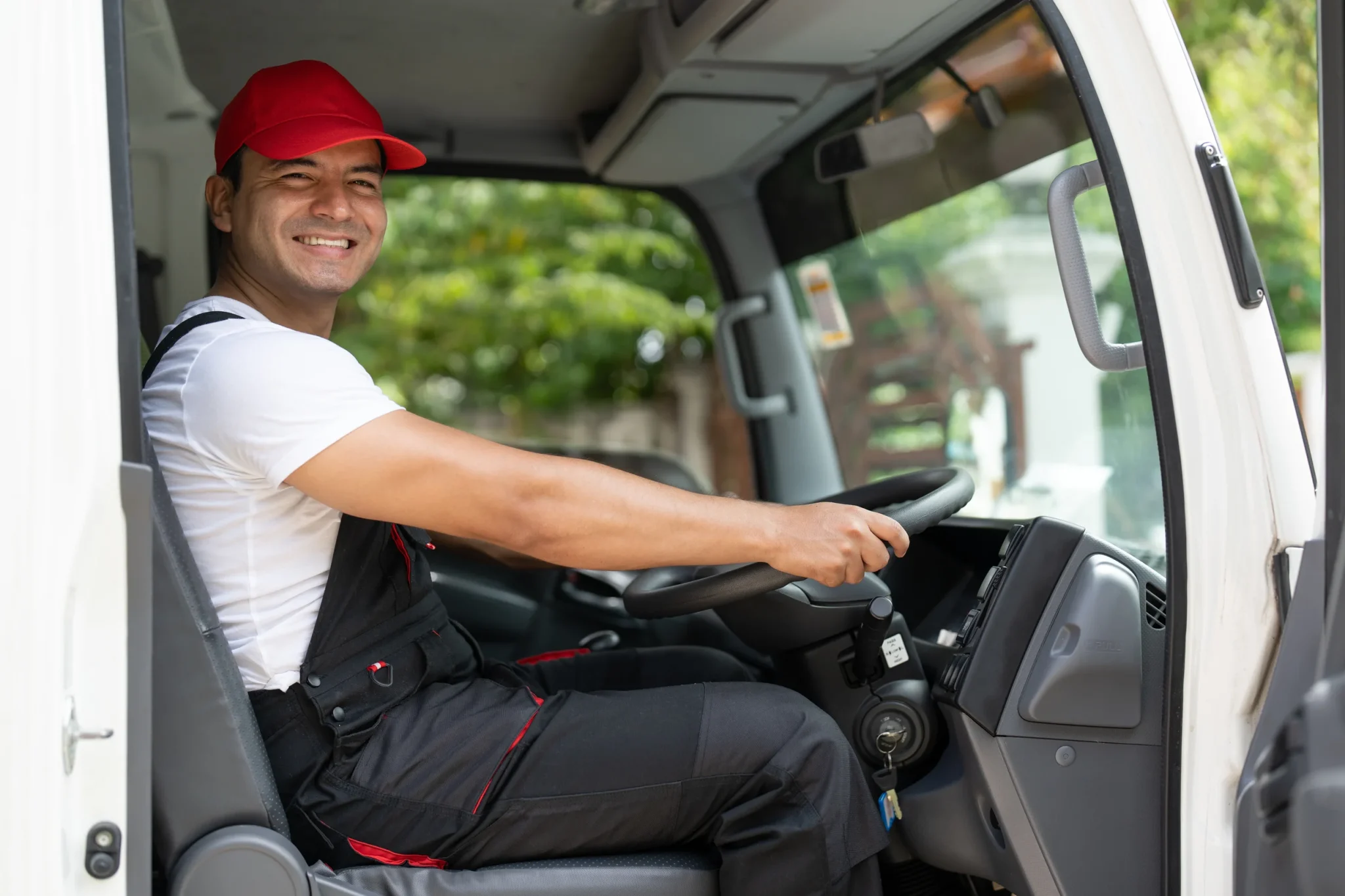 Smiling man wearing a red cap, sitting behind the wheel of a truck, enjoying the drive